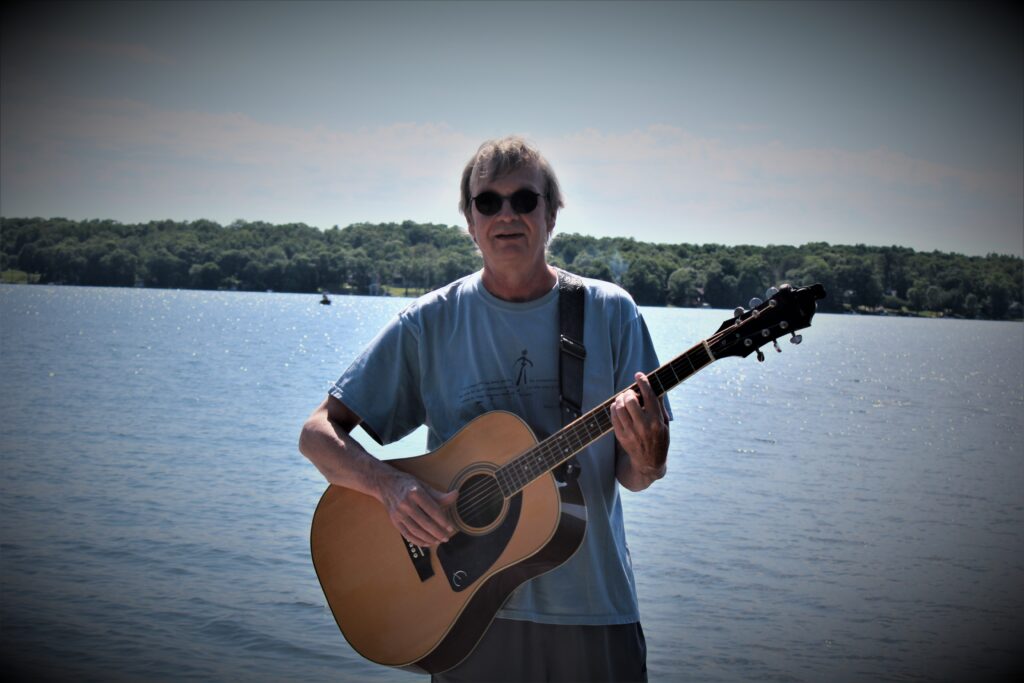 Nolen Chew Jr with a guitar next to a water body